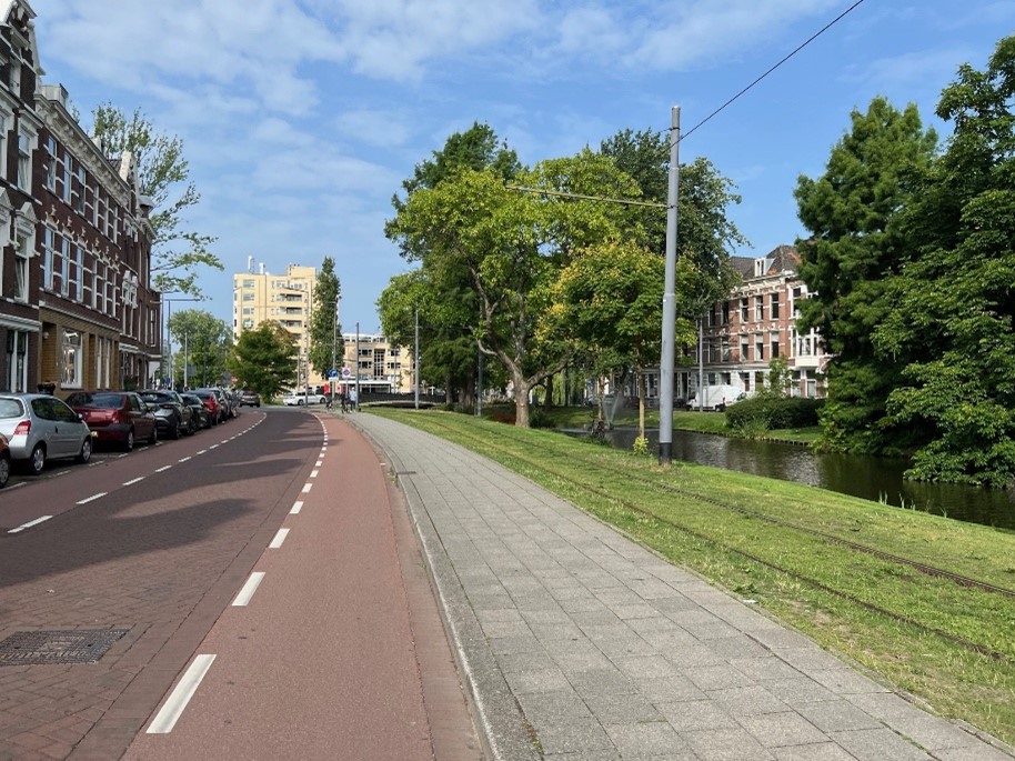 An image of a Dutch street that is shared between bicycles and motor vehicles, with on-street parking available. Bicycles travel in the shoulder to the right of a dashed line; vehicles keep right except to pass, where they move to the center of two dashed lines.